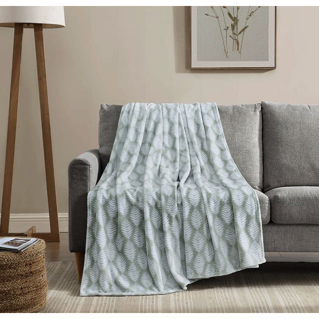 Social Standard by Sanctuary Oversized Plush Throw in light green and white leaf pattern draped over a grey fabric sofa, highlighting its wrinkle-resistant, machine washable microplush fabric designed for all-season softness and comfort in a neutral living room setting.