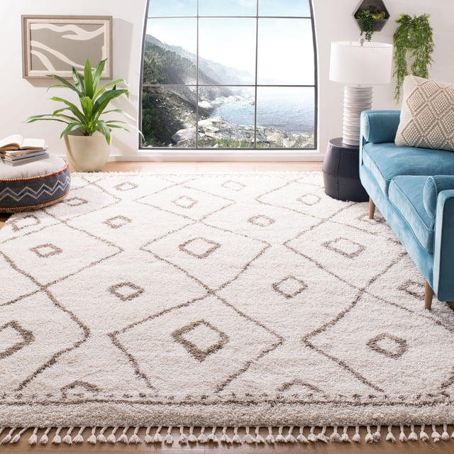 Safavieh Moroccan Fringe Barclay Geometric Shag Area Rug in a bright living space featuring a plush white synthetic yarn shag rug with brown geometric diamond patterns and fringed edges, placed near a blue sofa, a potted plant, and a large window with a coastal view, often used to add comfort and style to modern or country-chic interiors.