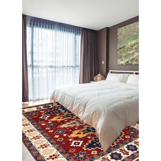 ECARPETGALLERY 100% Wool Traditional Indoor Area Rug for Entrance, Bedroom, Living Room and Dining Room featuring bold geometric Kazak patterns in red, yellow, blue, and cream tones, placed on a hardwood floor under a white bed in a bright bedroom with sheer curtains and taupe walls, ideal for adding warmth and style to indoor living spaces.