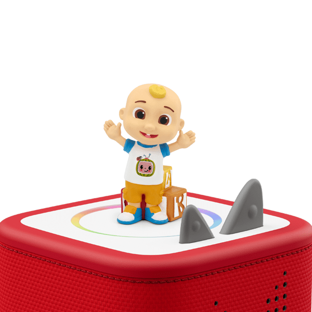 Tonies JJ Audio Play Character from CoComelon on a red Toniebox audio player with a white top featuring a multicolour circular design, showing JJ in a white shirt with a pink TV icon, orange shorts, and blue shoes, standing beside a wooden ABC block and two gray triangular controls.