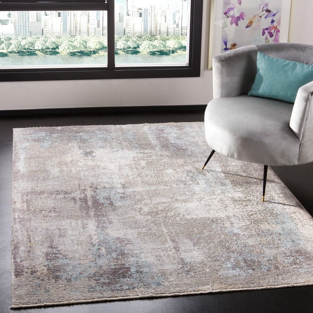 SAFAVIEH Dream Hamilton Abstract Overdyed Area Rug in beige, gray, and light blue abstract pattern on dark flooring under a gray armchair with teal cushion, near a large window with city and water view. This durable accent rug uses traditional Persian knotting, ideal for elegant home décor.