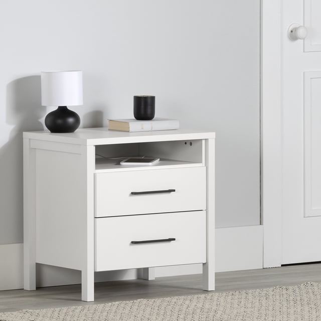 South Shore Gravity 2-Drawer Nightstand for Adult in pure white with two large drawers on metal slides and an open shelf holding a smartphone, featuring slim black handles and square legs, placed on a light wood floor against a grey wall with a black lamp and book on top, suitable for bedroom storage and bedside use.