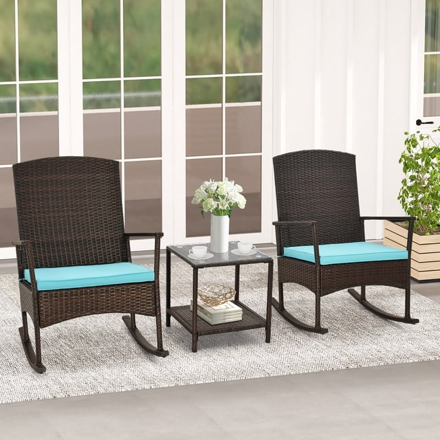 Gymax 3 Pieces Rocking Wicker Bistro Set featuring two mix brown PE rattan rocking chairs with turquoise cushions and a 2-tier side table with a tempered glass top. The set is displayed in an outdoor patio setting with a light rug and greenery in the background. The chairs include anti-slip stoppers for safety, and the table provides ample space for drinks and decor.