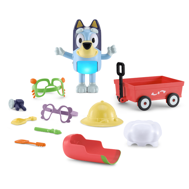 VTech® Bluey Dress-Up Bluey with Dress-Up Accessories and Wagon - English Version, 3-6 Yrs, featuring a front-facing Bluey figure with a glowing blue belly, nine colorful dress-up accessories including green and purple glasses, a yellow pith helmet, a red wagon with black handle, and small props for interactive pretend play and role-playing fun.