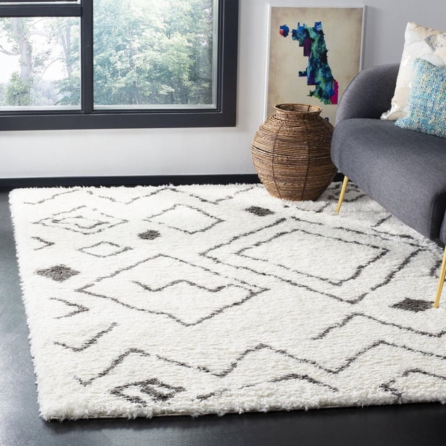 Safavieh Flokati Aiden Geometric Shag Area Rug in natural ivory with black geometric patterns, crafted from soft wool with a plush shag texture and durable cotton canvas backing, shown in a contemporary living room with a gray sofa, woven basket, and window overlooking greenery, ideal for adding warmth and style to bedrooms or living areas.