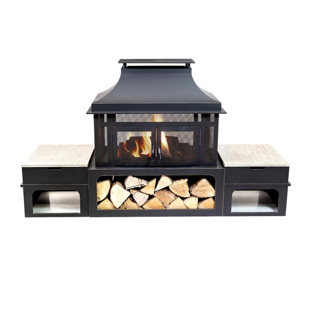 Deko Living 80 Inch Rectangular Outdoor Steel Wood Burning Fireplace with Log Storage, Poker and Side Tables featuring a matte black steel firebox with mesh doors showing burning logs, a curved chimney top, integrated log storage filled with split firewood below, and two side tables with light wood grain tops and open storage compartments, ideal for outdoor heating and gatherings.