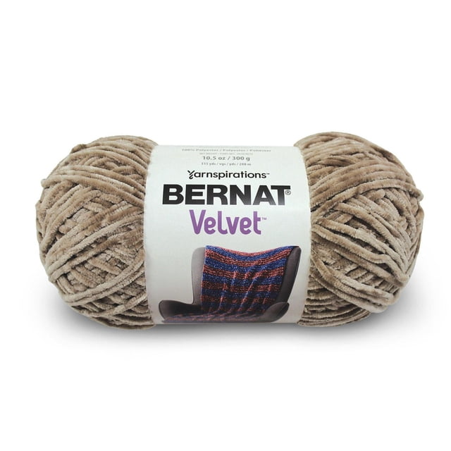 Bernat® Velvet™ Yarn, Polyester #5 Bulky, 10.5oz/300g, 315 Yards, beige plush velvet yarn skein with a white label showing the Bernat logo and an image of a knitted blanket on a chair, ideal for soft home decor knitting and crochet projects, often used for blankets and pillows.