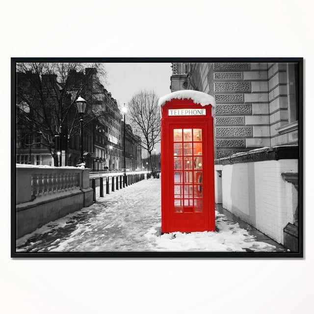 Design Art Red London Telephone Booth Framed Canvas Art Print depicting a centered red British telephone booth topped with snow, set against a black and white snowy London street with historic buildings and bare trees, printed on fade-resistant canvas stretched over a 1-inch wood sub frame and gallery-wrapped, arriving ready to hang with included hardware.
