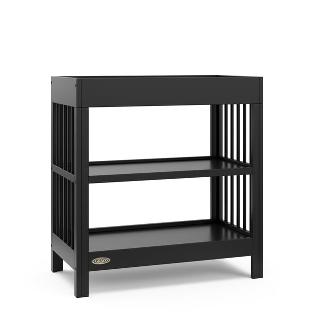 Graco Teddi Changing Table in black with two open storage shelves and a sturdy pine wood frame featuring vertical slats on the sides, includes a bonus water-resistant changing pad and safety strap, Baby Safety Alliance Verified for nursery use.