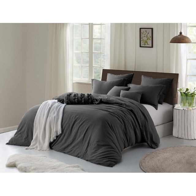 Natural Crinkle Fabric Ultra Soft Solid Duvet Cover Set - Zipper Closure in dark grey displayed on a bed with matching pillow shams, crafted from prewashed crinkle microfiber for softness. The set is styled with a white throw blanket in a bright bedroom featuring a wooden headboard, round woven rug, and white side table with a glass vase of flowers, illuminated by natural light through sheer curtains.