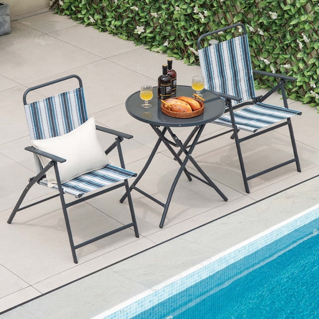Costway Ensemble de 3 Chaises de Salle à Manger Pliantes pour Patio, Métal Robuste et Portable pour l'Extérieur. l'Ensemble Comprend Deux Chaises Pliantes avec Tissu Respirant à Rayures Bleu et Blanc et Accoudoirs, et une Table Ronde Pliante avec Dessus en Verre Trempé. les Chaises et la Table Comportent un Cadre Métallique Robuste avec des Patins Antidérapants pour la Stabilité. l'Ensemble Est Exposé au Bord de la Piscine sur un Patio Carrelé avec de la Verdure en Arrière-Plan, Mettant en Valeur Sa Convenance pour la Détente et les Repas en Plein Air.