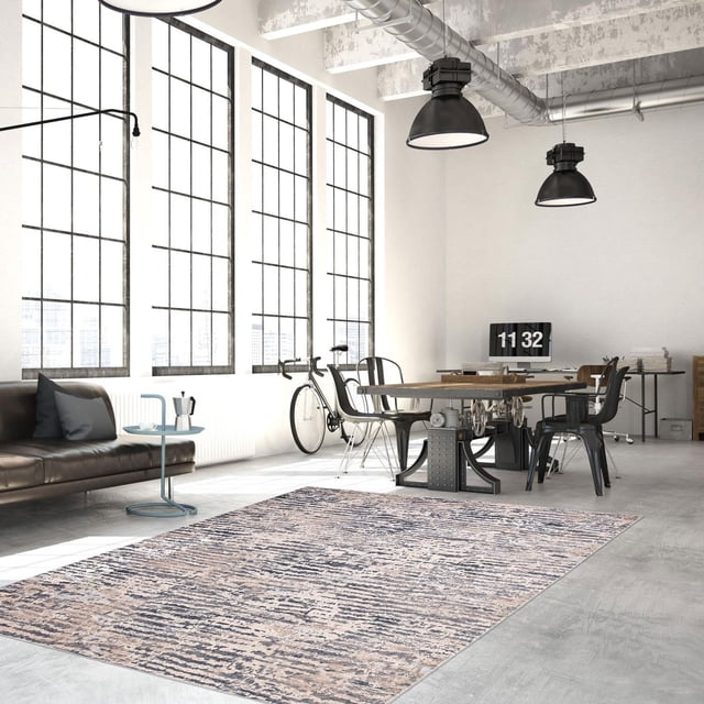 ECARPET Noelle Tapis Taupe avec Motif Abstrait Texturé Taupe et Gris dans un Bureau Industriel Lumineux avec Grandes Fenêtres à Grille, Planchers en Béton et Conduits Exposés. Positionné sous une table en Bois avec base en Métal et Chaises Noires, Près d'Un sofa en Cuir Noir et d'Une Bicyclette, Idéal pour un décor d'Espace de Travail Moderne.