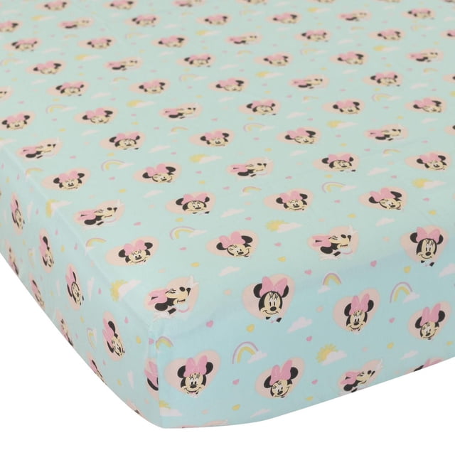 Disney fitted crib sheet with light blue background patterned with repeating Minnie Mouse faces wearing pink bows inside heart shapes, accented by small rainbows, clouds, and suns. Made of soft, breathable cotton, it fits standard crib mattresses measuring 28 by 52 inches plus 8-inch depth.