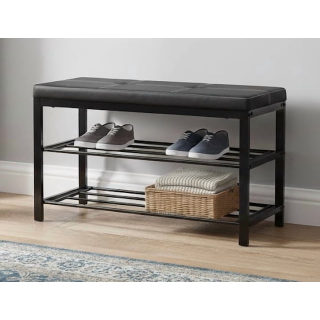 Nola Home 2-Tier Shoe Rack Bench with Padded Seat, featuring a black metal frame and a black faux-leather cushioned seat. The bench includes two open metal shelves, holding up to six pairs of shoes, with a basket and folded fabric displayed on the lower shelf. Compact and ideal for entryways, hallways, or mudrooms, it combines seating and storage in a sleek, modern design.