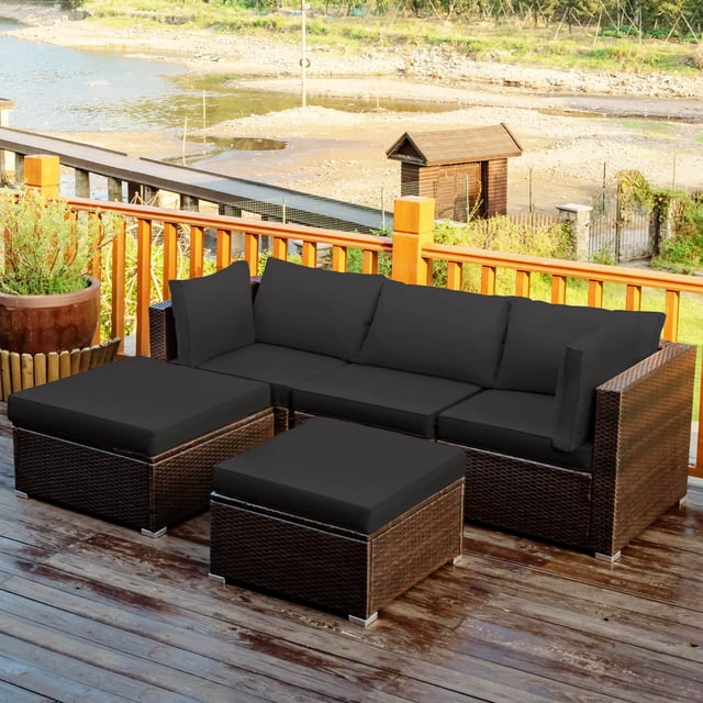 Costway 5PCS Outdoor Patio Rattan Furniture Set Sectional Conversation Black Cushion. This 5-piece set includes two corner sofas, one armless sofa, and two ottomans with black cushions. The furniture is made of weather-resistant PE rattan and a heavy-duty metal frame, designed for outdoor use. The ottomans can double as side tables when the cushions are removed. The set is displayed on a wooden patio overlooking a scenic outdoor area with a river and greenery.