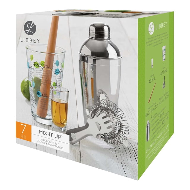MIX-IT-UP SET 7-piece mixologist bar tool set with stainless steel cocktail shaker, metal strainer with coil spring, wooden muddler inside a glass mixing cup printed with cocktail recipes, and a shot glass on a white wooden surface with a lime.