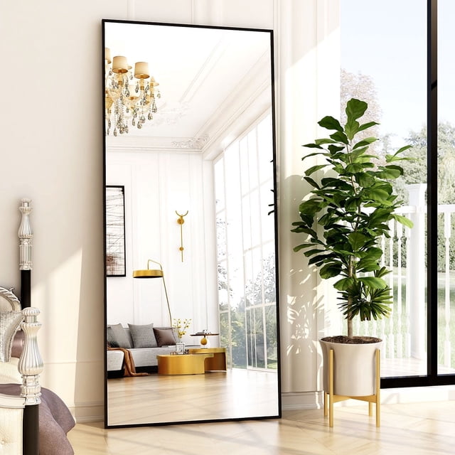 BEAUTYPEAK 76"x34" full length mirror with a rectangular shape and black aluminum alloy frame, featuring shatter-proof glass and HD imaging. Displayed leaning against a wall in a bright, elegant room, the mirror reflects a modern living space with a chandelier, gold accents, and a large potted plant. Suitable for leaning, standing, or wall mounting.