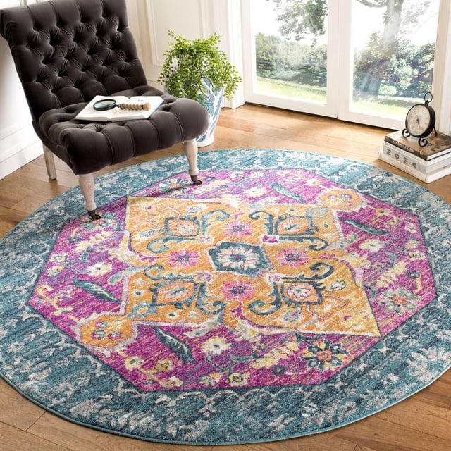 SAFAVIEH Madison Karissa Floral Area Rug, a round accent rug featuring a floral medallion pattern in yellow, pink, and teal on a teal border, power loomed with durable polypropylene yarns, displayed on hardwood floor beside a tufted dark gray chair, a potted plant, and a stack of books with a clock near a sunlit window, ideal for enhancing contemporary home decor.