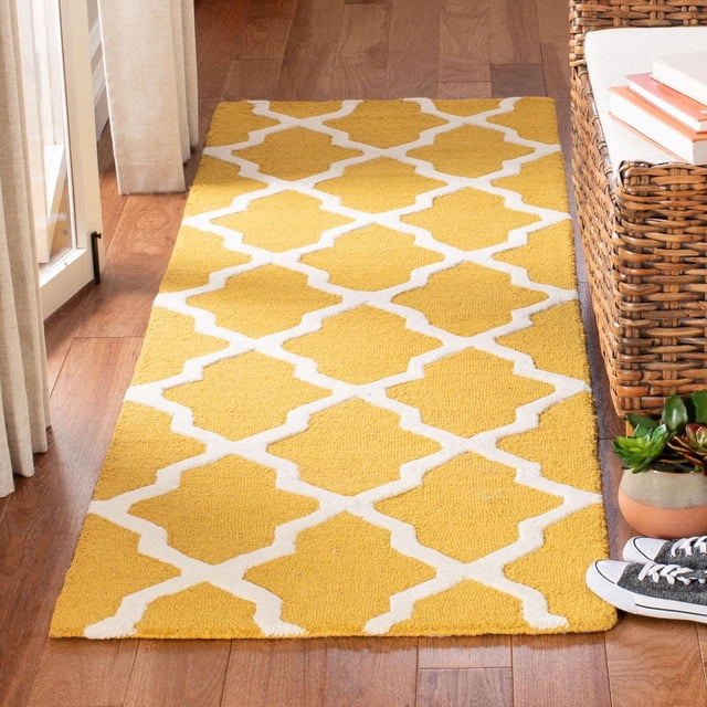 Safavieh Cambridge Liam Geometric Area Rug in yellow with white geometric lattice pattern, hand-tufted wool with plush cut pile and textured high/low loops, placed on hardwood floor beside wicker furniture and potted succulents, ideal for adding modern American style to home or office decor.