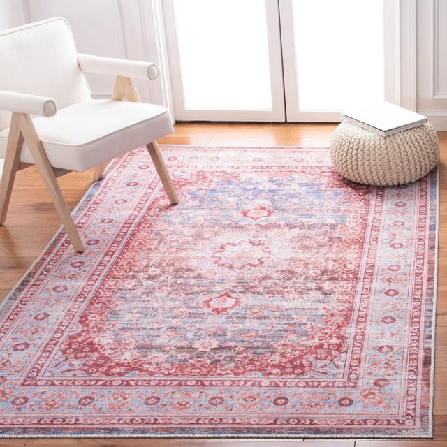 SAFAVIEH Serapi Chase Oriental Area Rug with a traditional oriental pattern in muted red, blue, and beige tones and a distressed finish, power loomed with a soft cotton, viscose, and polyester blend pile. Displayed on hardwood flooring beside a white modern armchair and a knitted beige pouf with a book, suitable for adding comfort and style to living spaces.