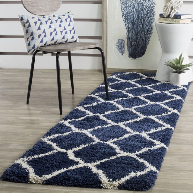 Safavieh Hudson Tapis Coureur à Motif Shag Géométrique Aligné pour Aire avec Motif Géométrique de Carreaux Marocains Bleu Marine et Blanc, Présentant une pile de Fil Synthétique Douce et durable sur un Plancher de Bois Clair à Côté d'Une Chaise Moderne avec un Coussin Géométrique Bleu et Blanc, une table d'Appoint Blanche avec des Livres et une Déco Corail, et art Corail Bleu Encadré, Convient pour Ajouter de la texture et de la Chaleur aux Couloirs Ou aux Entrées.