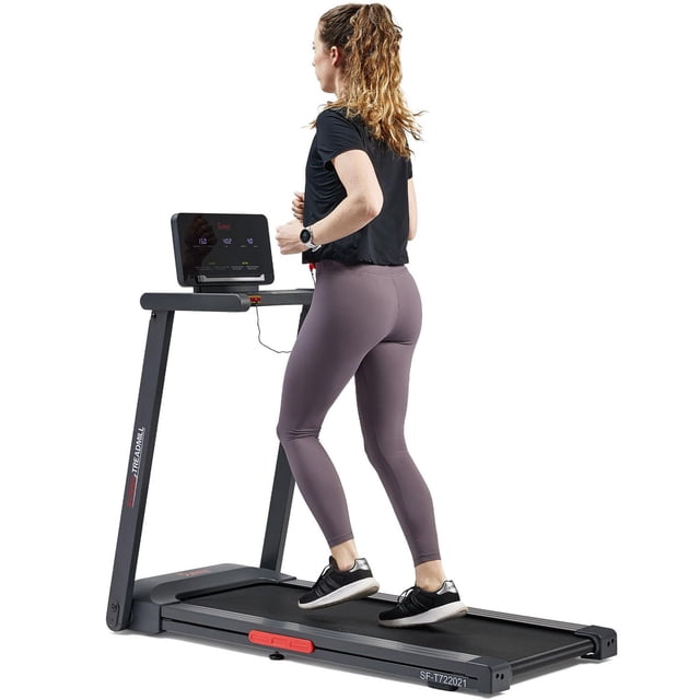 Sunny Health & Fitness Interactive Slim Folding Treadmill with Advanced Brushless Technology shown in side profile with a woman running, featuring a slim black frame, LED monitor displaying workout stats, folding design, and Bluetooth connectivity for SunnyFit app workouts.