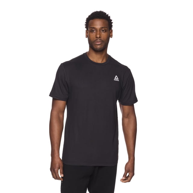 Reebok Men's Delta Core Short Sleeve Tee in black, front view on a male model. The athletic shirt features a crew neck, short sleeves, and soft, lightweight jersey fabric made of 94% polyester and 6% spandex. It has a fitted upper torso with a relaxed midsection and a white Reebok Delta logo on the left chest. Designed for moisture-wicking and all-day comfort, suitable for workouts and casual wear.