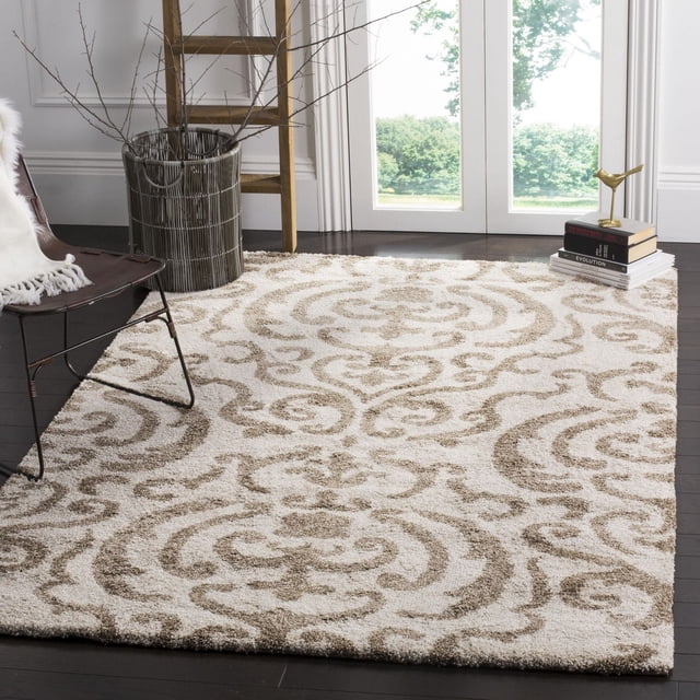 Safavieh Florida Deangelo Damask Plush Shag Area Rug with a plush, sculpted high-low pile in crème tone-on-tone damask vine pattern, set on dark hardwood floors in a bright room. Positioned near a modern chair, wooden ladder, and metal vase with bare branches, it adds texture and softness, ideal for living rooms or bedrooms.