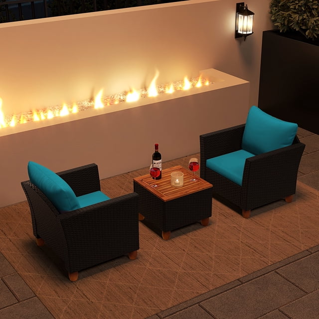 Costway 3PCS Patio Rattan Furniture Set with two cushioned armchairs featuring turquoise cushions and a storage coffee table with a solid acacia wood top. Perfect for outdoor patios, porches, or gardens, the set is shown in a cozy patio setting with a fire feature and ambient lighting.