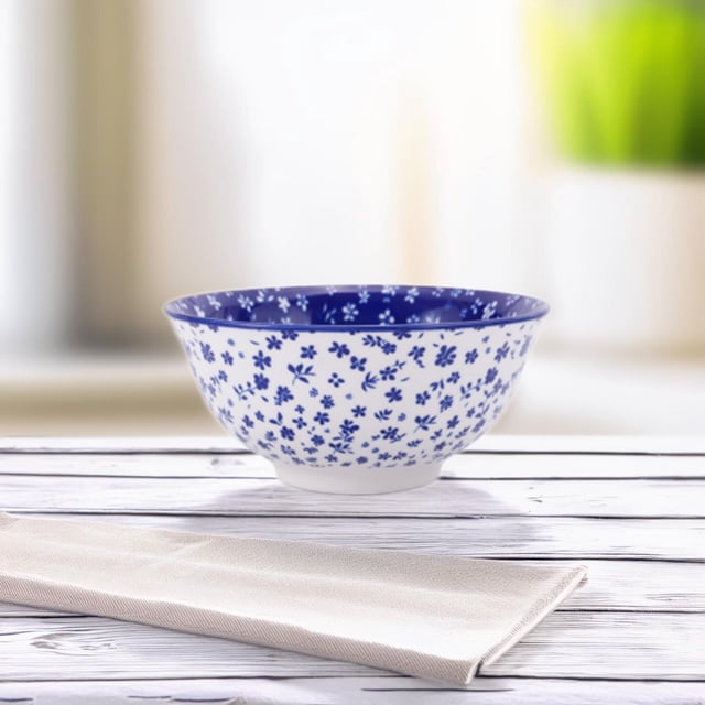 Mainstays 4.5" pad printed bowl with white stoneware exterior decorated in blue floral patterns and a solid blue interior, shown on a white wooden surface with a beige napkin, ideal for salads or everyday meals and safe for dishwasher and microwave use.