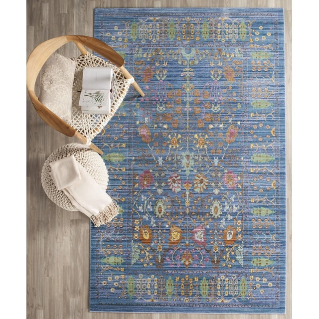 Safavieh Valencia Tapis Traditionnel Grigor Bleu Mettant en Vedette des motifs Floraux et Géométriques Persans Traditionnels Richement Saturés en Or, Vert, Rose et Brun sur une surface Texturée Surteinte, Exposé sur un Plancher de Bois Clair à Côté d'Une Chaise Tissée avec un Coussin beige et un Livre Ouvert, et un pouf Tricoté Crème avec un Jeté beige Plié, Souvent Utilisé pour Ajouter un style Classique et de la Chaleur aux Espaces de Vie.