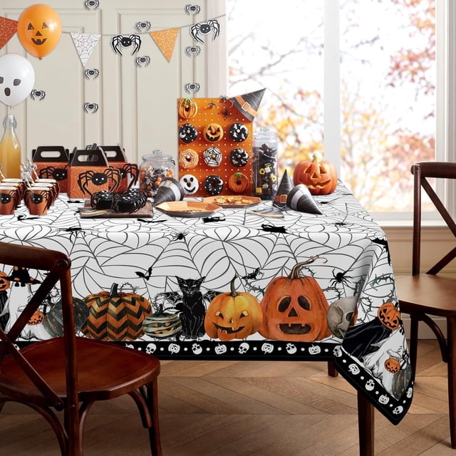 Halloween Spider Web Tablecloth Rectangle, measuring 60 x 84 inches, displayed on a dining table. The tablecloth features a white background with black spider web patterns, bordered with Halloween-themed graphics including pumpkins, black cats, bats, skulls, and ghosts. The table is set with Halloween party decor, such as orange and black cups, treat boxes, and carved pumpkins, creating a festive atmosphere. Suitable for tables seating 6-8 people, made from 100% polyester fabric that is waterproof, washable, and wrinkle-free.