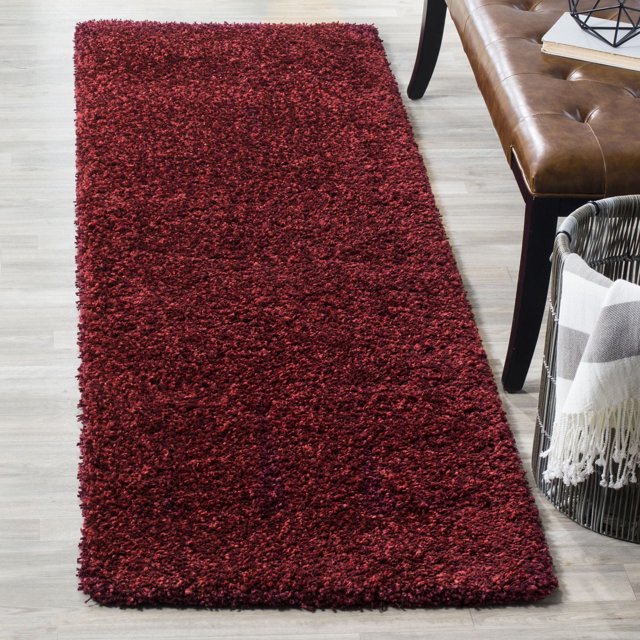 Safavieh California Solid Plush Shag Area Rug in deep red with a super dense 4.5kg per square meter polypropylene pile, shown on light wood flooring beside a brown leather bench and a woven basket with a striped throw, suitable for adding plush softness and warmth to home spaces.