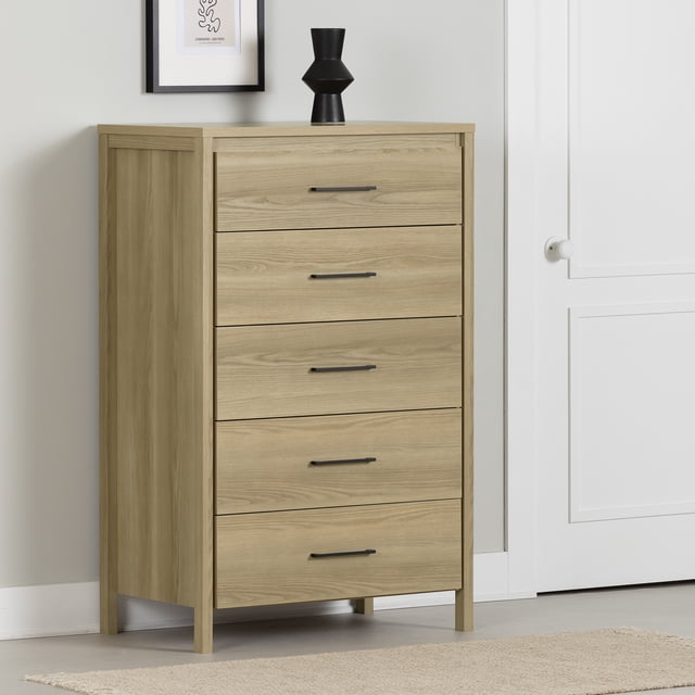 South Shore Gravity 5-Drawer Chest for Adult in natural ash finish, a tall, narrow dresser with five wide drawers featuring slim black handles and squared legs, placed in a minimalist room with light grey walls and a white door, topped with a black vase and framed abstract art, ideal for small bedroom storage and organizing clothes.