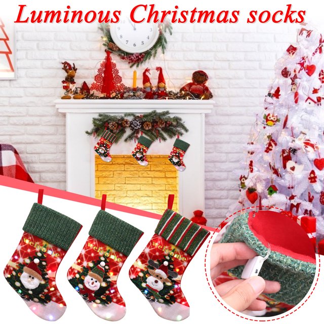 Vaidha LED Illuminated Large Christmas Stocking Christmas Decorations featuring a set of three stockings with Santa, snowman, and reindeer designs. Made of non-woven fabric, these red and green stockings include bright LED lights and a sturdy hanging loop. Displayed in a festive indoor setting with a fireplace and Christmas tree, they are ideal for holding candy canes, chocolates, and small gifts. Perfect for hanging on walls, doors, or fireplaces during the holiday season.