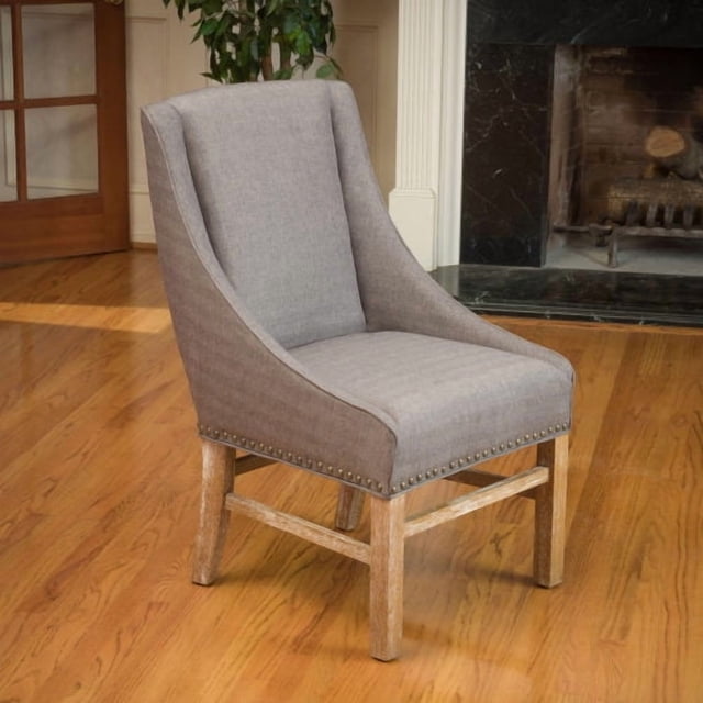 Mid-Century Dining Chair - Handmade Nailhead Trim (Brown Gray) with plush brown-gray upholstery, tapered wooden legs, and individually applied nailhead accents. Ideal for dining seating or kitchen furniture, the chair is displayed on a hardwood floor in a cozy room with a fireplace and greenery in the background.