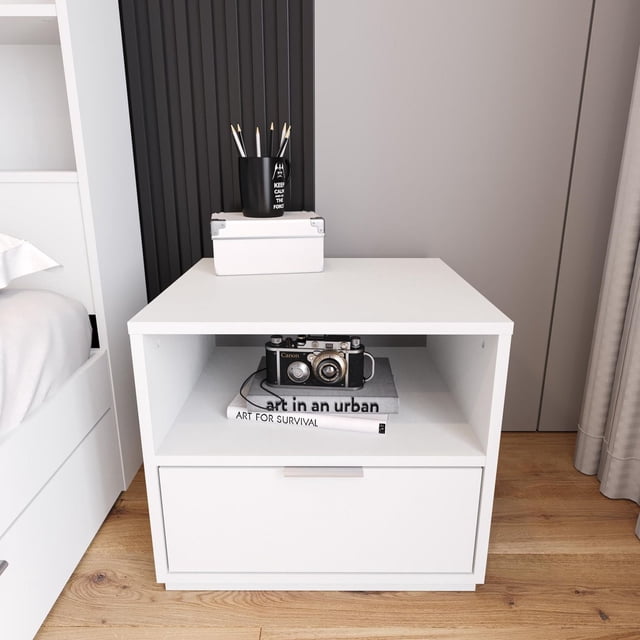 Nexera Hunter Nightstand with 1 Drawer in white, showing an open shelf with a vintage Canon camera and two art books, topped with a white box and black pencil holder with pencils, on a wooden floor beside a bed. This bedroom furniture piece provides discreet storage and display space ideal for organizing essentials.