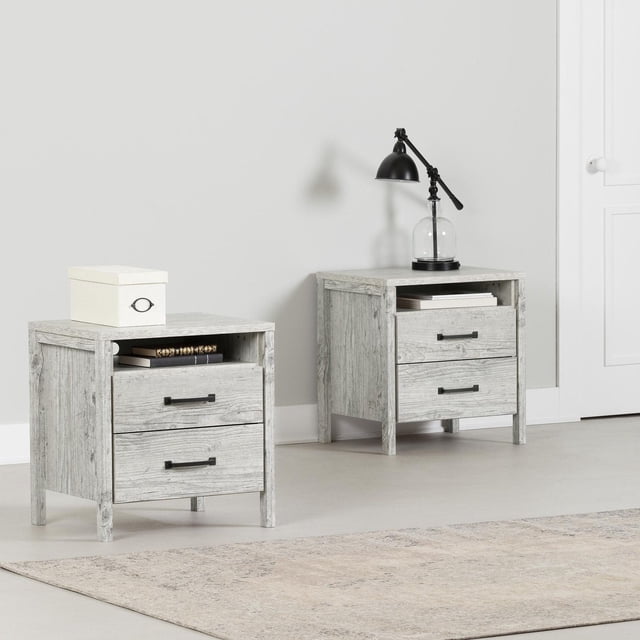 South Shore Gravity Ensemble de 2 Tables de Nuit pour Adulte, Fini Pin Bord de Mer, Comprenant Deux Tables de Nuit Identiques avec Deux Grands Tiroirs sur Chemins en Métal, un Compartiment Ouvert pour Livres, Poignées Droites Noires et Pieds Droits, Présenté dans une Chambre Neutre avec un Tapis beige, une Boîte de Rangement Blanche sur l'Un, et une Lampe Noire Ajustable sur l'Autre, Idéal pour Organiser Vêtements et Accessoires.