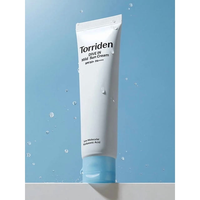 Torriden Dive-In Mild Sun Cream 60ml tube with white body and light blue cap, labeled SPF50+ PA++++ and low molecular hyaluronic acid, standing upright on a white surface with water droplets around it against a light blue background, providing gentle, moisturizing broad-spectrum sun protection ideal for daily use.
