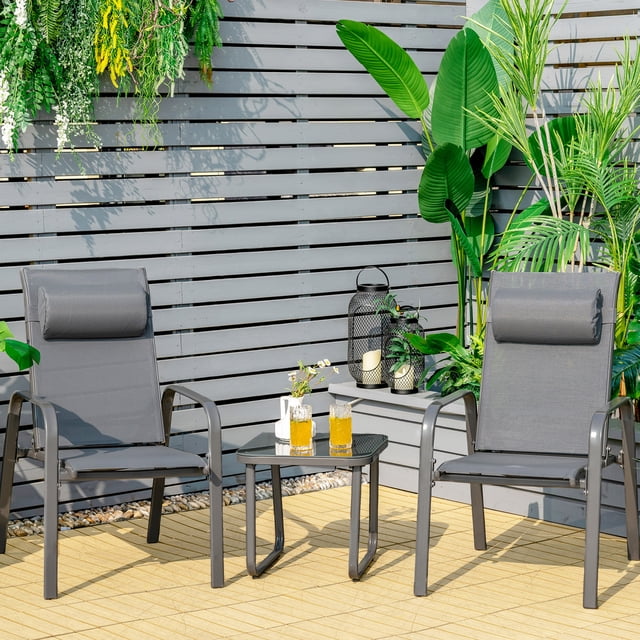 Gymax Ensemble Bistro d'Extérieur 3 Pcs Ensemble de Conversation pour Patio en Gris, Comprenant Deux Chaises Empilables avec Dossiers et Appuie-Têtes Ajustables, et une table Basse en Verre Trempé avec Patins Antidérapants. les Chaises Sont Faites d'Acier Inoxydable et de Tissu à Séchage Rapide, Convenant aux Espaces Extérieurs Compacts comme les patios Ou les Balcons. l'Ensemble Est Exposé sur une Terrasse en Bois Entourée de Verdure Luxuriante.
