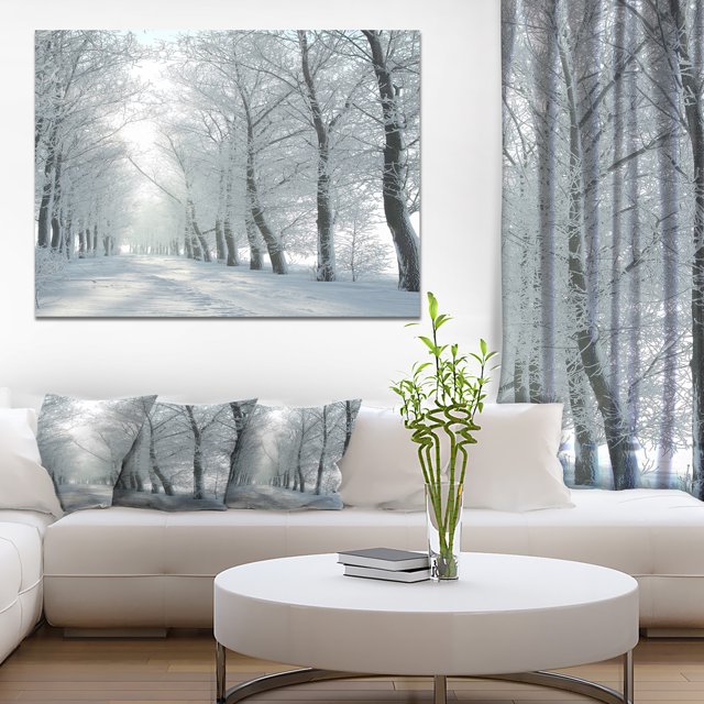 Winter Country Lane on Frosty Morning - Large Forest Canvas Art Print displayed in a modern living room setting. This wall art features a tranquil winter landscape with snow-covered trees along a country lane, printed on premium cotton canvas with fade-resistant ink. The gallery-wrapped design continues on the sides, stretched over a 1-inch wood subframe for durability. Ideal for home décor, the canvas arrives ready to hang with included hanging kits.