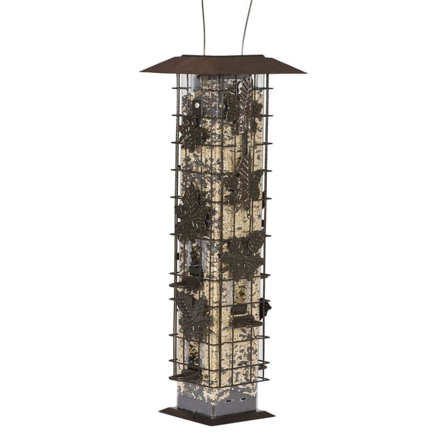 Perky-Pet Squirrel-Be-Gone Wild Bird Feeder with a clear vertical seed reservoir enclosed by a powder-coated metal cage featuring decorative leaf designs, six feeding ports with U-shaped perches, and a weight-activated system that closes ports to deter squirrels, suitable for hanging in outdoor garden spaces.