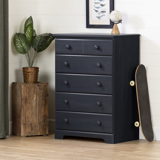 South Shore Summer Breeze 5-Drawer Chest for Child in Blueberry, front view showing five smooth-gliding drawers with round wooden knobs and a decorative groove on the top drawer, set against a white shiplap wall with a framed fish print and a globe on top, a skateboard leaning on the right, and a potted plant on a rustic wooden stand to the left, suitable for organizing kids' clothing and toys in a bedroom.