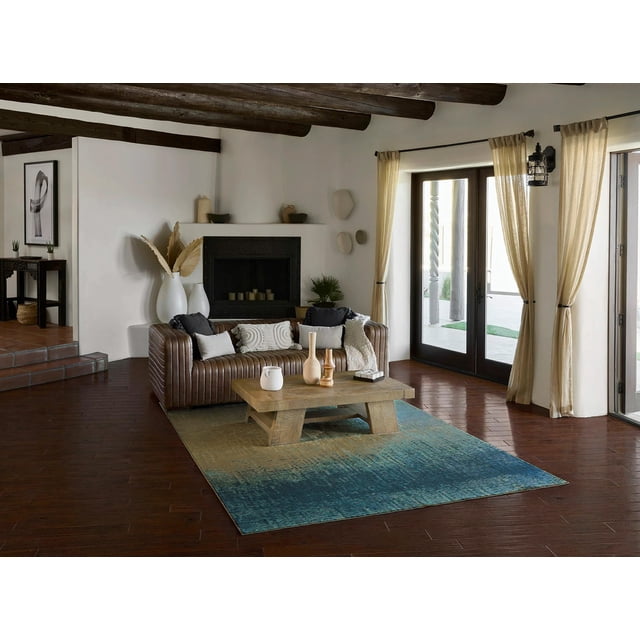 ECARPET Sable Contemporary Area Rug for Living Room, Bedroom, Dining Room, Entrance, Hallway and More with a rectangular beige to teal color-washed gradient under a wooden coffee table in a living room featuring dark hardwood floors, a brown leather sofa with textured pillows, beige curtains on glass doors, and a white fireplace with decorative vases. The rug’s light polyester pile suits multiple home areas.