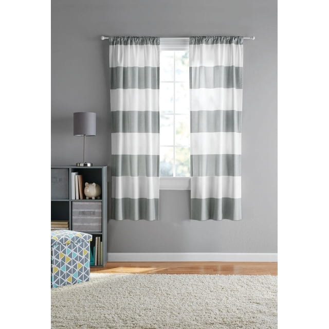 Mainstays Cabana Stripe 84" Rod Pocket Window Panel Pair in silver and white wide horizontal stripes hanging on a white rod over a window in a grey room with hardwood floor, grey lamp on a cubed shelf, and a geometric patterned storage ottoman on a white shag rug, suitable for adding classic striped style to bedrooms or living spaces.