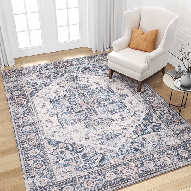 SIXHOME 8'x10' Area Rugs for Living Room in a vintage medallion design with distressed light blue tones. The rug features a soft low pile and intricate patterns, creating a cozy and elegant atmosphere. It is placed in a bright living room with a white armchair, an orange accent pillow, and a side table. The rug has a TPR rubber backing for anti-skid properties and is machine washable for easy maintenance.