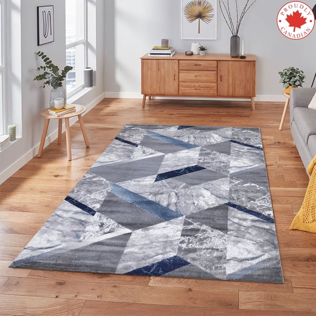 A2Z Paris 1989 Contemporary Living Room Marble Abstract Triangular Pattern Area Rug displayed in a modern living room with wooden flooring. The rug features a geometric design with shades of grey, white, and navy blue, creating a marble effect. It is made of 100% heat-set polypropylene with a 10mm low pile thickness and a jute hessian backing for durability. Suitable for living rooms, bedrooms, dining rooms, and hallways, this rug adds a stylish and cozy touch to any space.