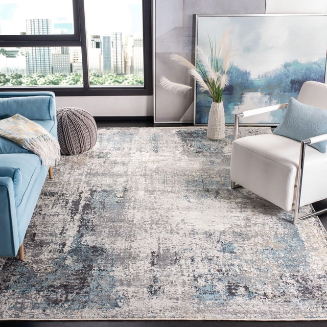 SAFAVIEH Dream Hamilton Abstract Overdyed Area Rug 8'x10' with a distressed abstract pattern in blue, grey, and cream tones, placed in a modern living room under a light blue sofa, grey knitted pouf, and white armchair with a blue cushion. A white vase with pampas grass and a large abstract painting lean against the wall near a window showing a city skyline. The durable power-loomed rug is ideal for adding a designer chic upgrade to home décor.