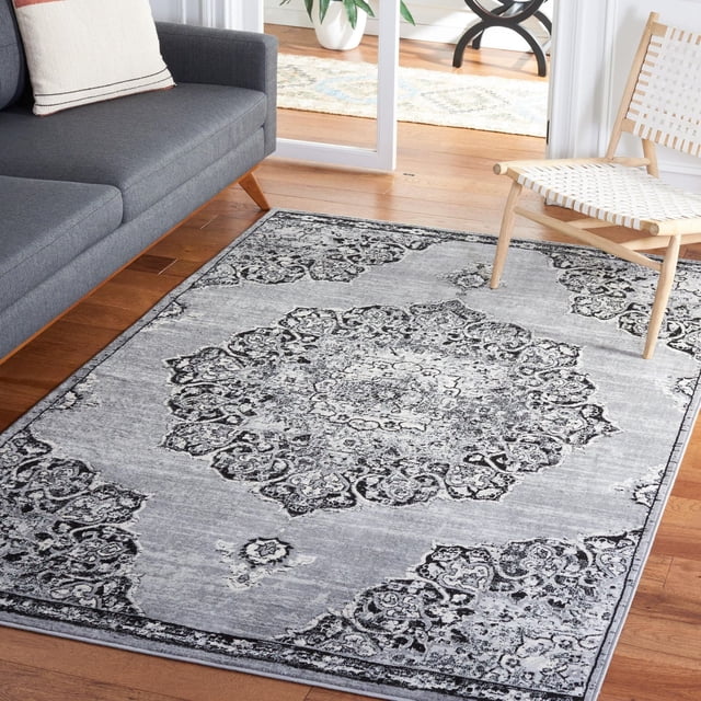 SAFAVIEH Brentwood Dimitri Floral Bordered Area Rug in grey with a central floral medallion and intricate border pattern, made from soft synthetic yarns in a close cut pile, displayed on hardwood flooring between a grey sofa and a woven white chair in a bright living room, ideal for traditional and transitional decor.