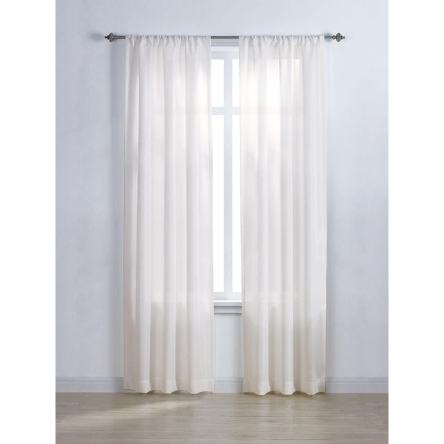 Mainstays Tille 63" solid rod pocket window curtains panel in white, hanging on a metal rod over a window with cross muntins, made of sheer polyester fabric that gently filters light while enhancing privacy, set in a minimalist room with light wood flooring and white walls, suitable for layering with other window treatments.